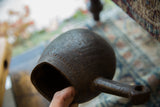 Holding the vintage Sudanese wooden pitcher to show its dark, aged texture and form.