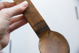Hand-carved lines and aged patina on the handle of a vintage wooden spoon.