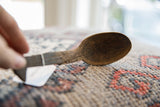 Angled view of the vintage wooden spoon's dark, hand-carved texture and bowl.