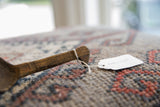 The aged wooden handle of a vintage African spoon with its paper tag attached.
