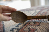 Aged wood grain and rough, hand-carved texture of the vintage African spoon's bowl.