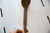 A full-length overhead view of a vintage African wooden spoon showing its inventory tag.