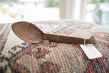 Angled view of a vintage African spoon, showing the shallow bowl and carved handle details.