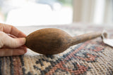A hand holding the vintage wooden spoon to feature its aged, textured bowl.