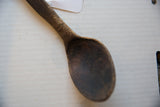 Aged patina and character marks on the dark, hand-carved bowl of a wooden spoon.