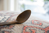 Aged texture and a small crack on the dark wood bowl of a vintage spoon.