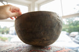A hand holds the thick, rustic rim of the vintage wooden bowl for scale.