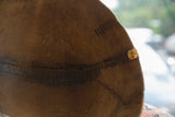 Detail of a dark, hand-stitched repair and metal patch on the aged wooden bowl.
