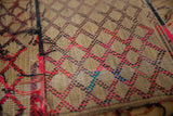 Close-up of the vintage Tuareg mat's handwoven straw texture with red, black, and blue diamond pattern.