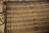 Wrapped edge and handwoven straw texture with dark lines and reddish patterns on a vintage Tuareg mat.