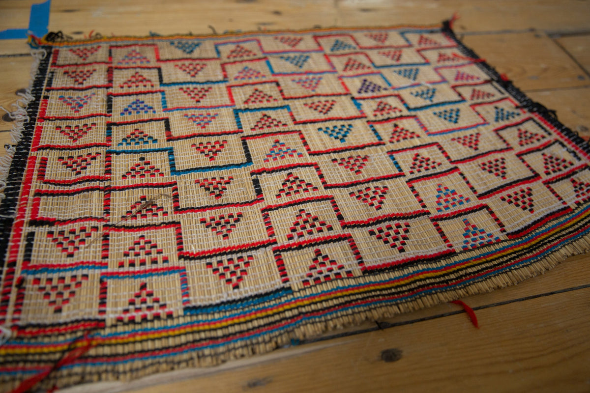 Vintage Tuareg straw mat with a geometric grid of red, blue, and black pyramid designs.