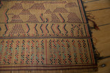 Vintage Tuareg mat close-up: handwoven straw texture, geometric red, black, and teal squares.