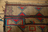 Detail of a vintage handwoven Tuareg straw mat showcasing red, blue, and black geometric patterns.
