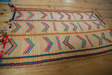 Angled view of a vintage Tuareg mat's handwoven straw and colorful geometric patterns.