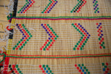 Close-up of a Tuareg mat's edge, detailing the handwoven straw and multicolor yarn.