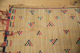 Woven straw texture of a Tuareg mat with red, black, and teal geometric motifs.