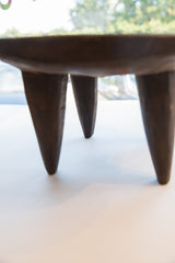 Low angle detail of the African Senufo wood milk stool's hand-carved dark legs.