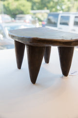 Vintage African Senufo wood stool with dark, hand-carved texture on its tapered legs.