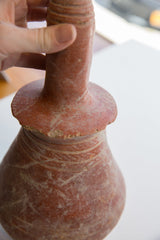 A hand holds the antique red slip ware vase by its ribbed, slender neck.