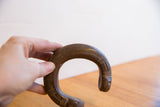 Antique African snake cuff bracelet held in hand, showing its curved shape and etched patterns.