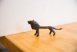 The vintage African lion sculpture's slender body and textured dark patina in profile.