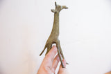 Low-angle view of the vintage oxidized giraffe sculpture, showing its textured form and slender legs.