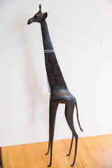 The slender, elongated form of a vintage African giraffe collectible with a dark patina.