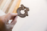 Curved form and dark, textured patina of a vintage double chameleon pendant.