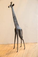 The slender, stylized form of a vintage African giraffe sculpture in dark, textured metal.