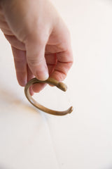 Antique African bronze snake cuff held to show its C-shape and handmade form.