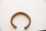 Aged copper alloy cuff bracelet showing its open C-shape and rounded ends.
