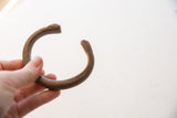 The solid, curved form of an antique copper alloy cuff bracelet held in hand.