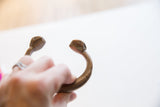 The open ends of the antique bronze snake cuff with stylized, carved head details.