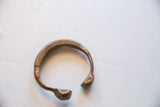 The open C-shape and stylized snake-head ends of an antique African bronze cuff.