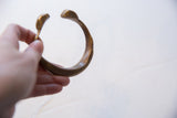 The open C-shape and aged patina of the antique bronze snake cuff bracelet.