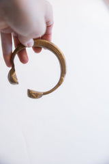 Hand holding an antique bronze snake cuff to show its curved profile.