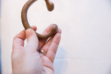 A hand holding the antique bronze snake cuff, showing its C-shape and ribbed texture.