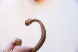 Aged patina on the smooth snake head and ribbed body of the bronze cuff.