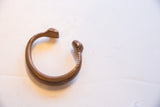 The curved form and warm patina of the antique African copper alloy snake cuff.