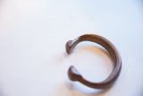Profile of the antique copper alloy bracelet, highlighting its curved form and stylized open ends.