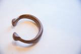 The curved profile and flared end of an antique African copper alloy snake cuff bracelet.