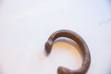 The rounded head and ribbed texture of the antique African snake cuff.