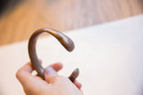 The open C-shape and smooth, rounded terminals of the antique copper alloy bracelet.