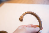 Incised markings and aged patina on the terminal of a copper snake cuff.