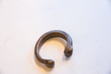 The curved form and faintly engraved surface of the antique bronze cuff.
