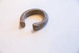 The open form of a thick, antique bronze cuff with chiseled details on its ends.