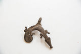 Aged metallic patina and stylized lizard form of a collectible African pendant.