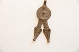 Detailed form of a vintage African pendant showing textural aged metal and stylized heads.