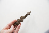 Vintage African pendant with a wavy shape and aged patina held in hand.