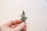 Hand holding the vintage bronze crocodile pendant, showing textured back and spiral motifs.
